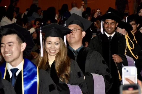 Graduates in regalia walking down an aisle