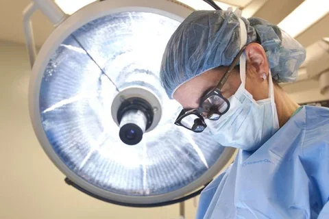 Photo of Doctor in surgery with surgical lamp behind them 