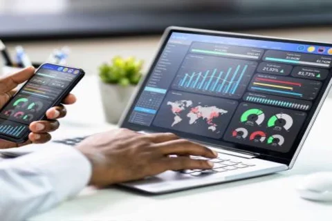 close up of a laptop screen and a hand holding a phone displaying the same charts and data