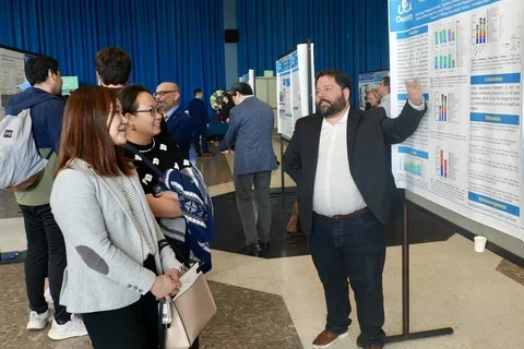 Man in suit explaining research poster to two women