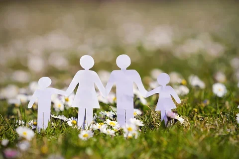 paper bodies of family holding hands over grass and flowers in spring