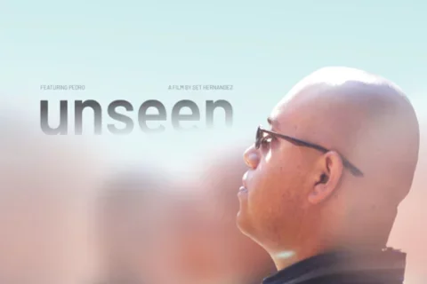 A bald young man appears in-focus, amidst hazy figures surrounding him. He wears glasses while looking up to the endless bright sky above him, his expression pensive. As the sky meets the young man’s head in the middle of the poster, the film’s title appears: unseen.