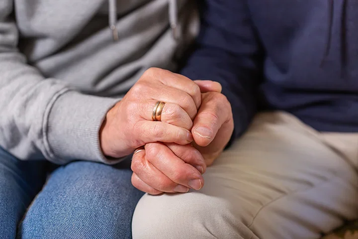 Spouse holding hands resting on legs