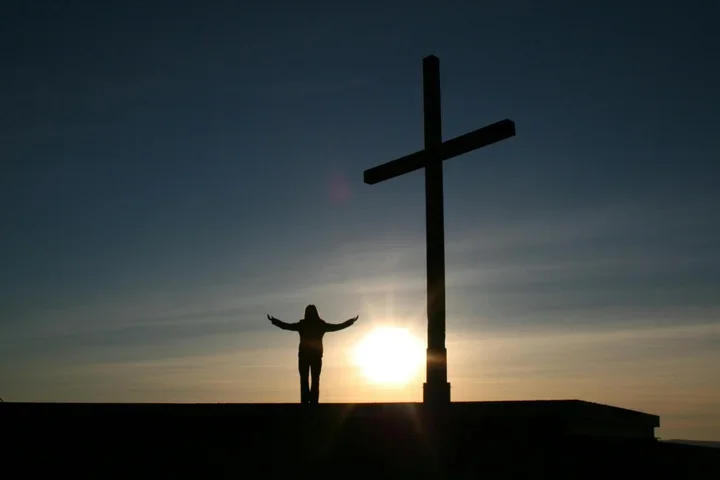 silhouette of a person standing next to a large cross with the sun behind them