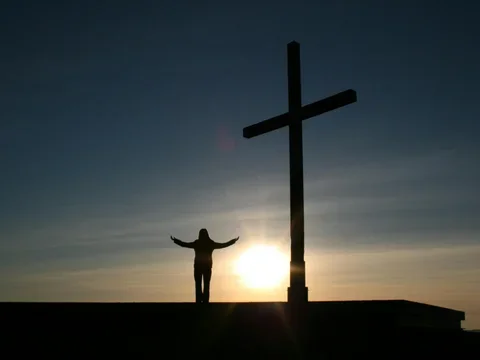 silhouette of a person standing next to a large cross with the sun behind them