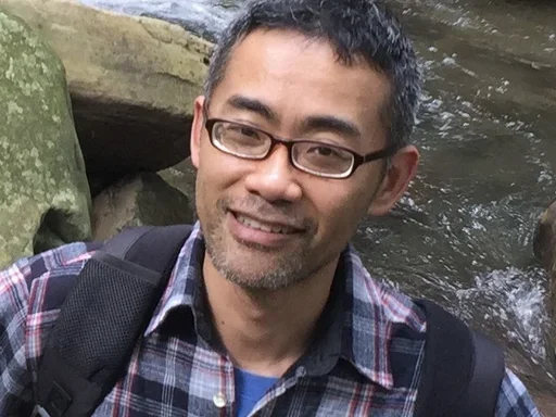 Man with glasses and collar-plaid shirt with river in the background